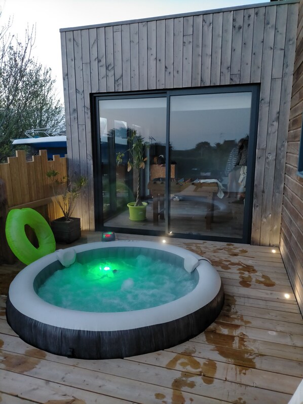 A wooden deck with a hot tub, a wooden fence, and a glass door leading to a patio area.