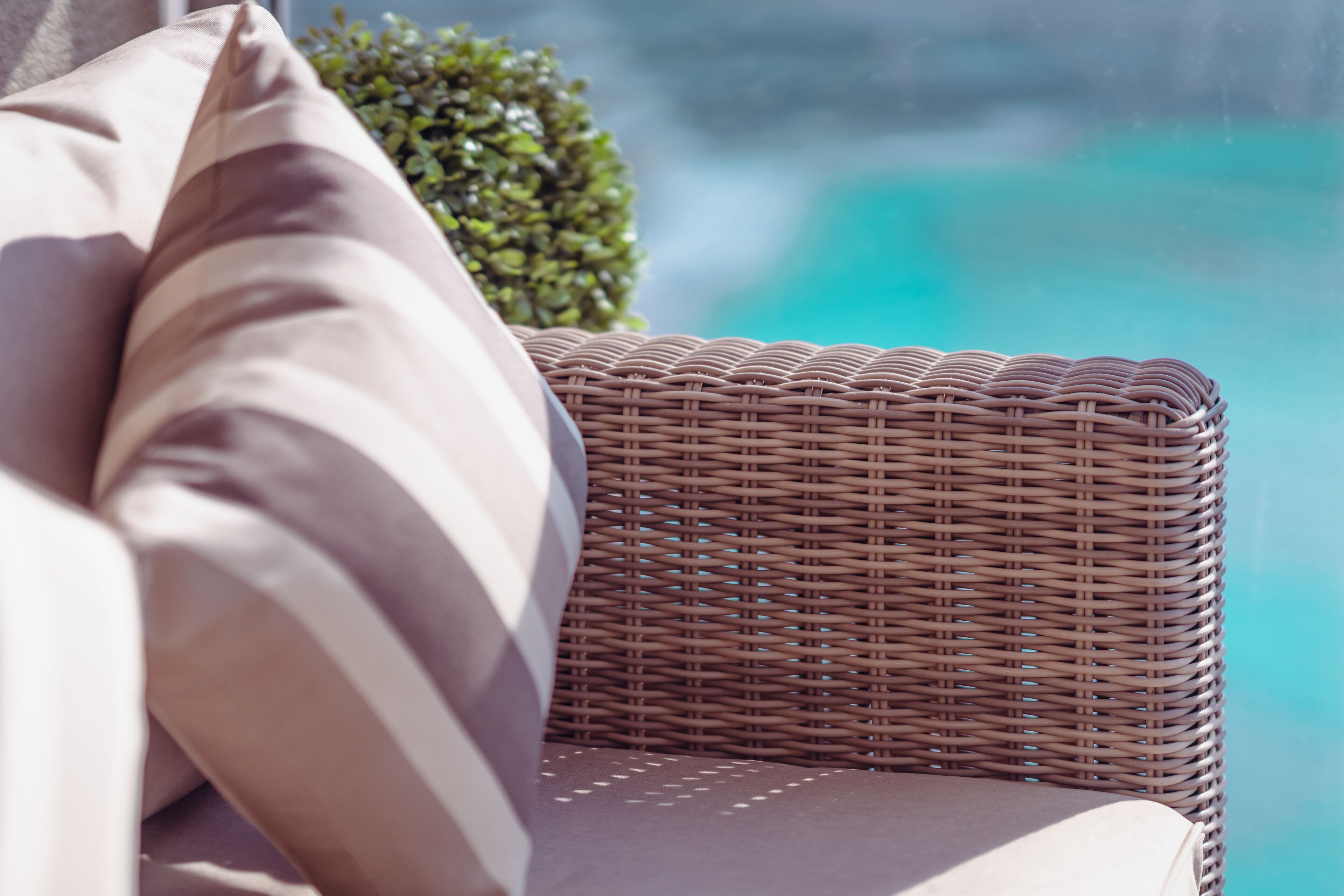 A wicker chair with a cushion, positioned near a window overlooking a body of water.
