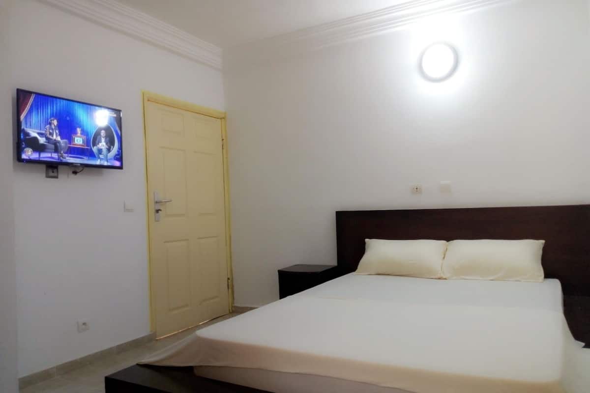 Een slaapkamer met een bed, een aan de muur bevestigde televisie, een deur en een nachtkastje.