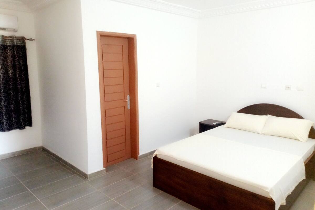 Een slaapkamer met een bed, een houten deur, een klein nachtkastje en een gordijn.