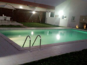 A swimming pool with metal ladders, surrounded by a tiled deck and a grassy area. - Hôtel Naell Assinie (Assinie)