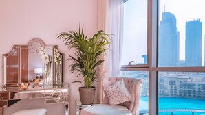 Een slaapkamer met uitzicht op de stad, een kaptafel met spiegel, een plant en een comfortabele fauteuil.