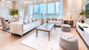 A modern living room with a sofa, ottomans, a coffee table, and a view of the city through large windows.