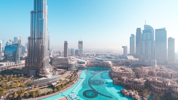 A high-rise building with a modern design, surrounded by a water feature and other buildings. - Elite Royal Apartment - Burj Khalifa & Fountain view - Royal (Dubai)