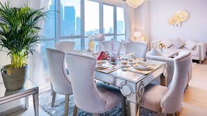 A modern dining area with a glass table, white chairs, and a city view through large windows. - Elite Royal Apartment - Burj Khalifa & Fountain view - Royal (Dubai)
