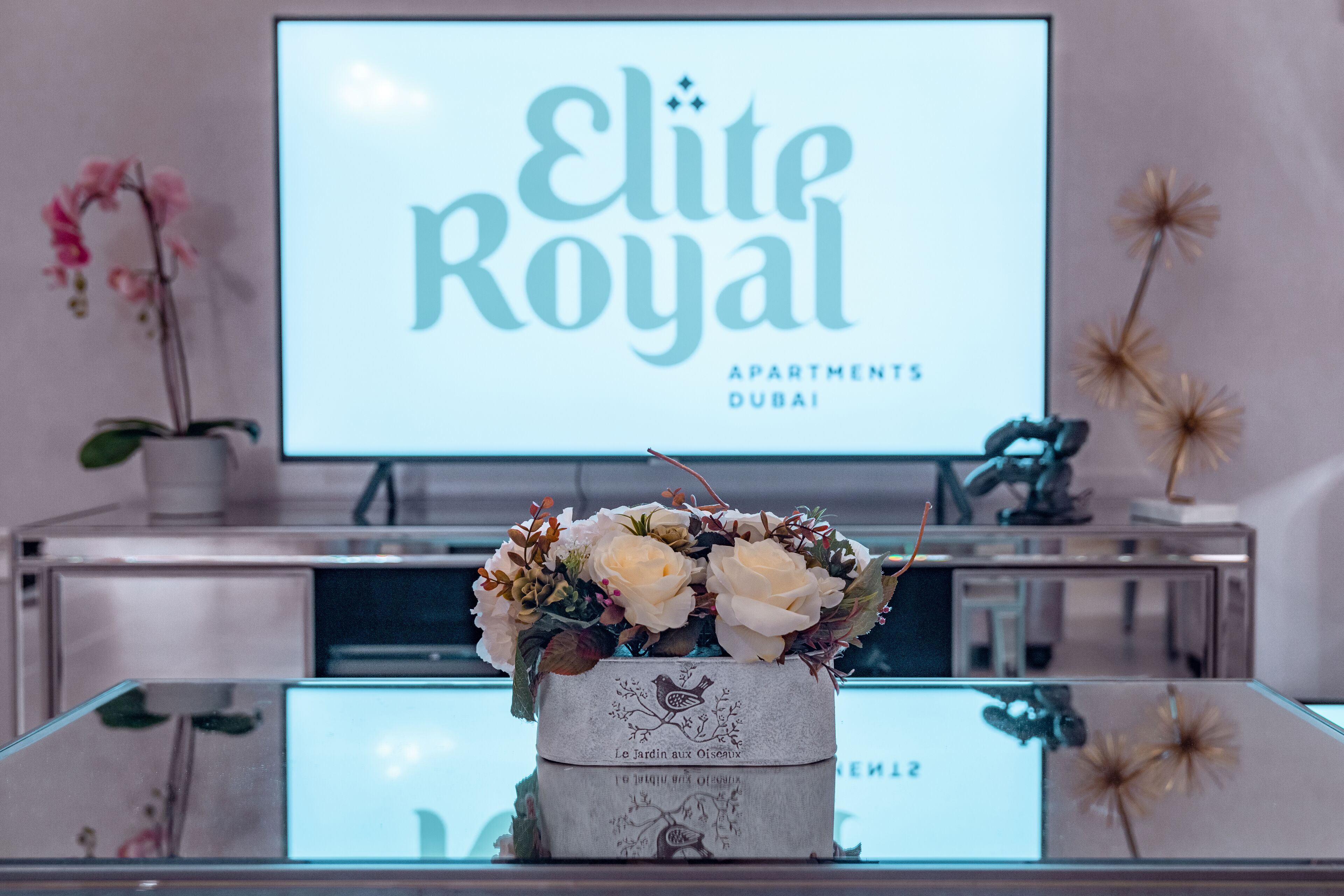 A floral arrangement on a table with a sign in the background reading "Elite Royal Apartments Dubai".