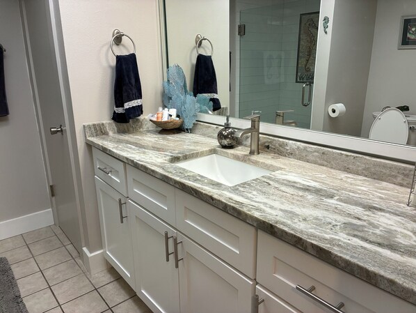 A bathroom with a marble sink, white cabinets, and a large mirror.