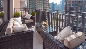 Ein Balkon mit Korbmöbeln, einem Glastisch und Blumentöpfen.