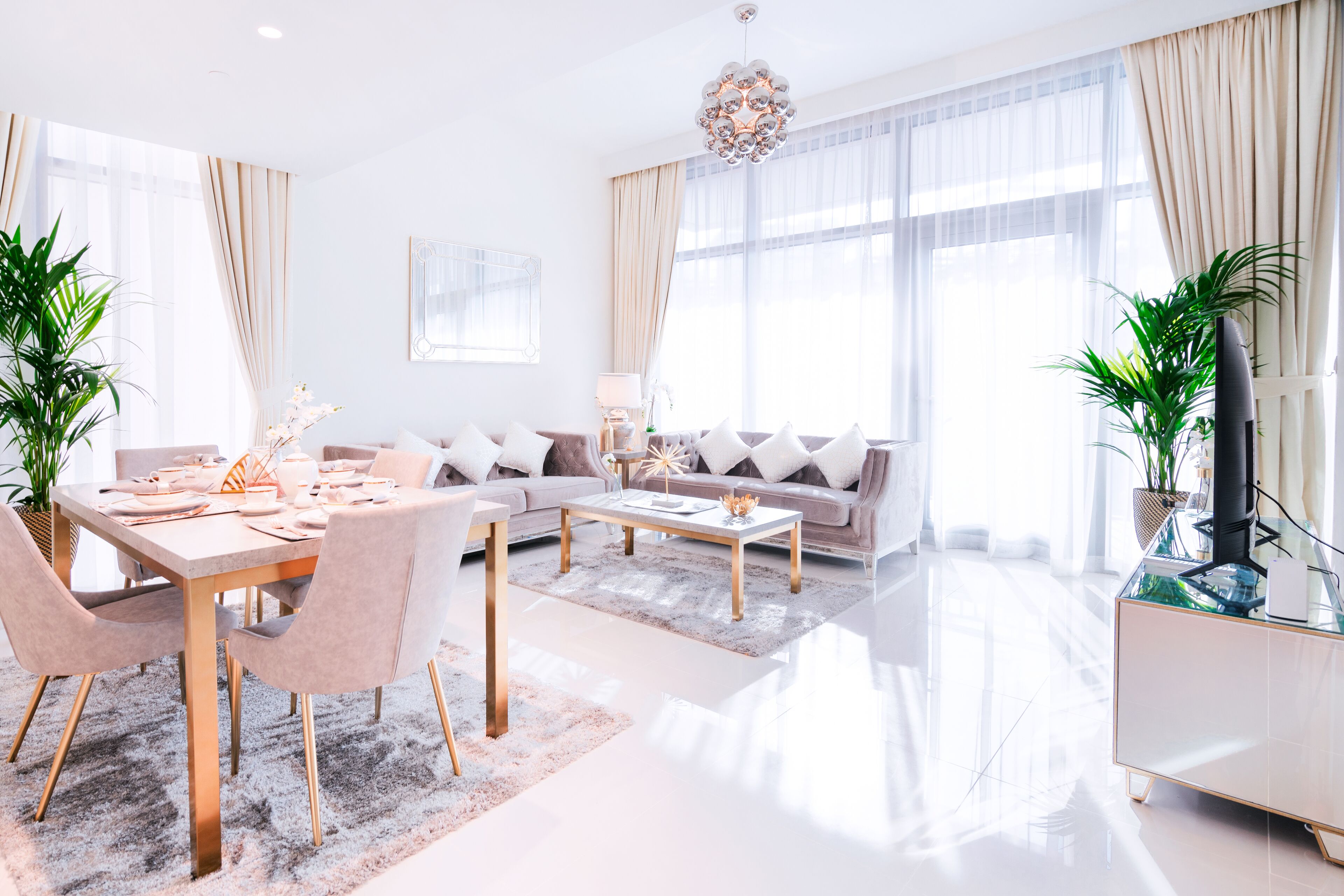 A modern living room with a dining area, large windows, and a chandelier.
