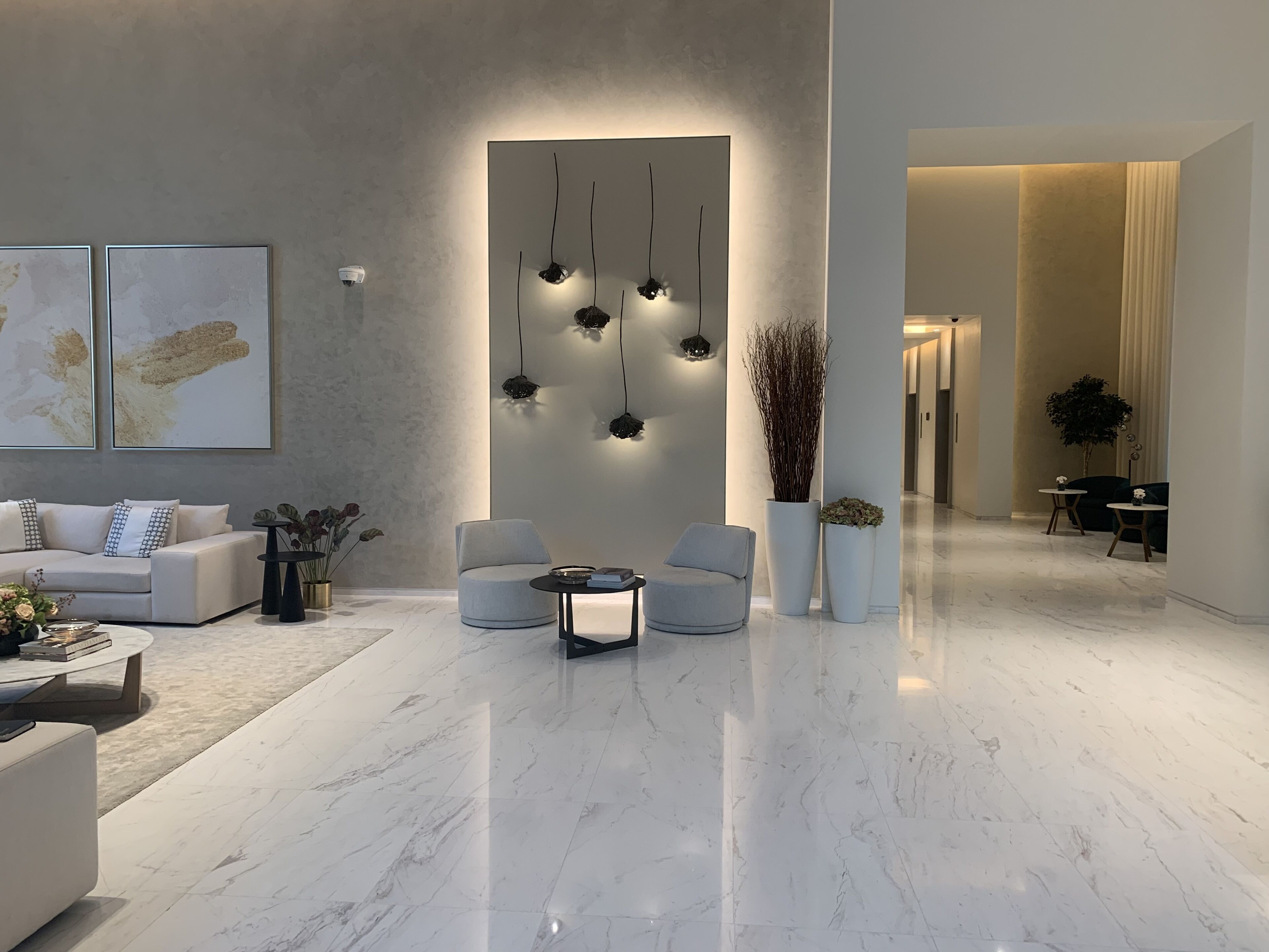 Een moderne woonkamer met een marmeren vloer, een bank, twee fauteuils, een salontafel en een wandlamp.