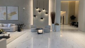 Ein modernes Wohnzimmer mit Marmorboden, einer Couch, zwei Sesseln, einem Couchtisch und einer Wandleuchte.