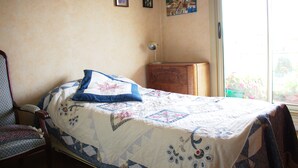 A bedroom with a bed, a chair, a wooden cabinet, and a window with a view of greenery. - COMFORTABLE 4/5-ROOM APARTMENT IN SECURE RESIDENCE WITH SWIMMING POOL (Saint-Raphaël)