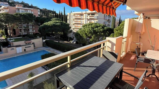 A balcony with a pool, outdoor furniture, and a view of the surrounding buildings and greenery. - COMFORTABLE 4/5-ROOM APARTMENT IN SECURE RESIDENCE WITH SWIMMING POOL (Saint-Raphaël)