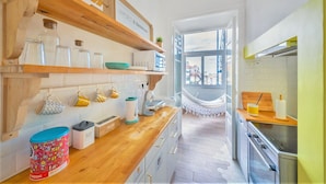 A modern kitchen with wooden shelves, a hammock, and a view of buildings through a large window. - Family Dream | A/C | Balcony & View | Lofts | Desk (Lisboa)