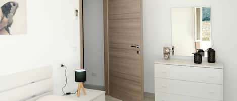 A modern bedroom with a wooden door, a white dresser with decorative items, a bedside lamp, and a wall-mounted air conditioner.