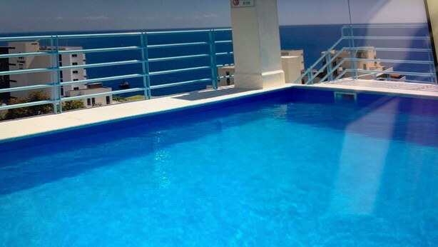 Une piscine d’un bleu éclatant, avec vue sur la mer et des bâtiments en arrière-plan.