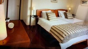 Une chambre d’hôtel avec un lit double, deux tables de chevet, une petite table d’appoint, une petite plante en pot et une porte.