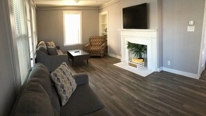 Ein Wohnzimmer mit einer Couch, einem Sessel, einem Couchtisch, einem Kamin und einem flachbildfernseher, der darüber angebracht ist.