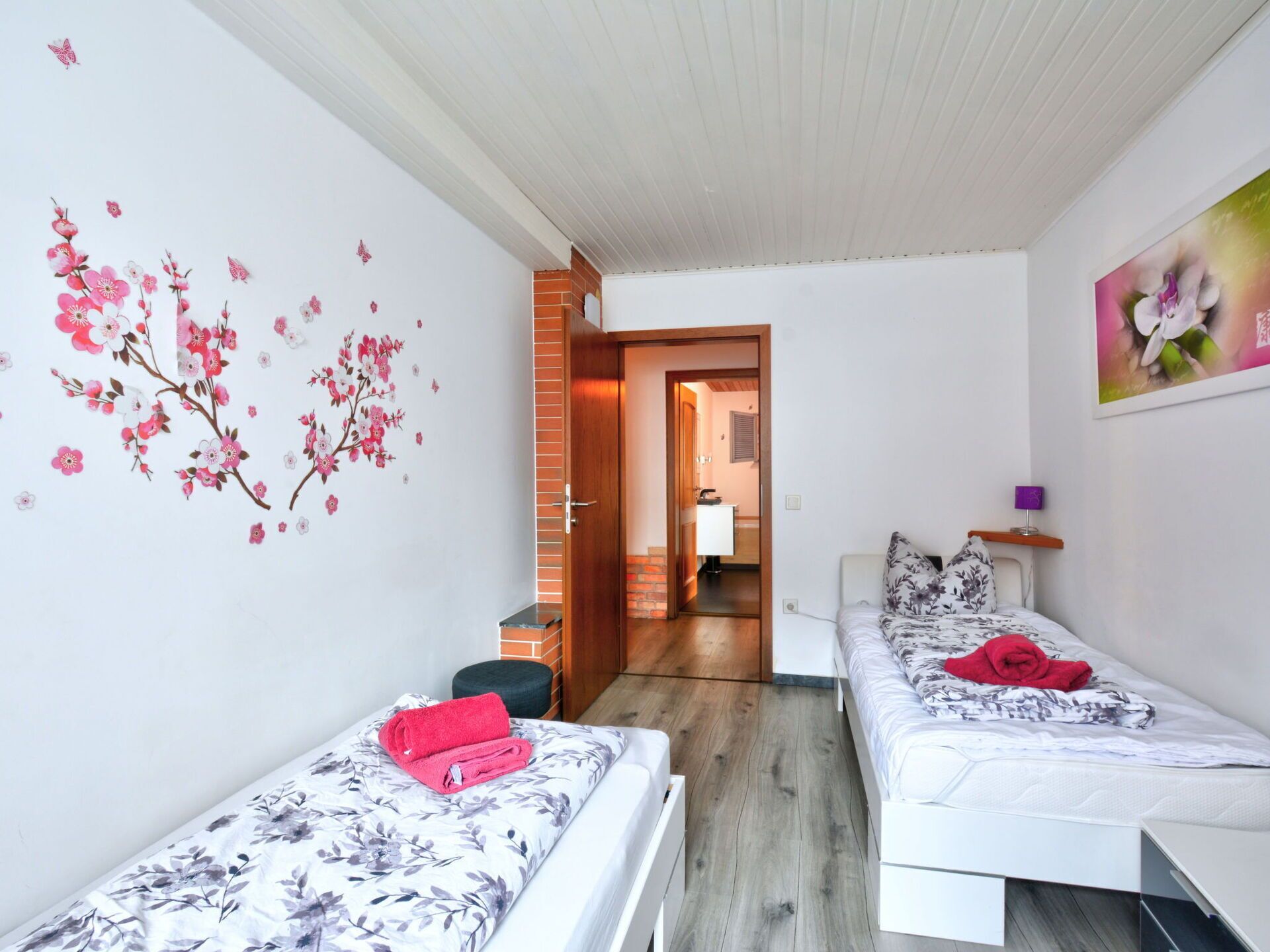 Una habitación pequeña y luminosa con dos camas individuales, piso de madera y pared de ladrillo.
