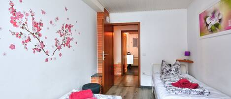 Una habitación pequeña y luminosa con dos camas individuales, piso de madera y pared de ladrillo.