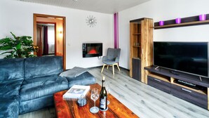 Ein modernes Wohnzimmer mit einer Couch, einem Couchtisch mit Flasche und Glas, einem Fernseher und einem Holzschrank.