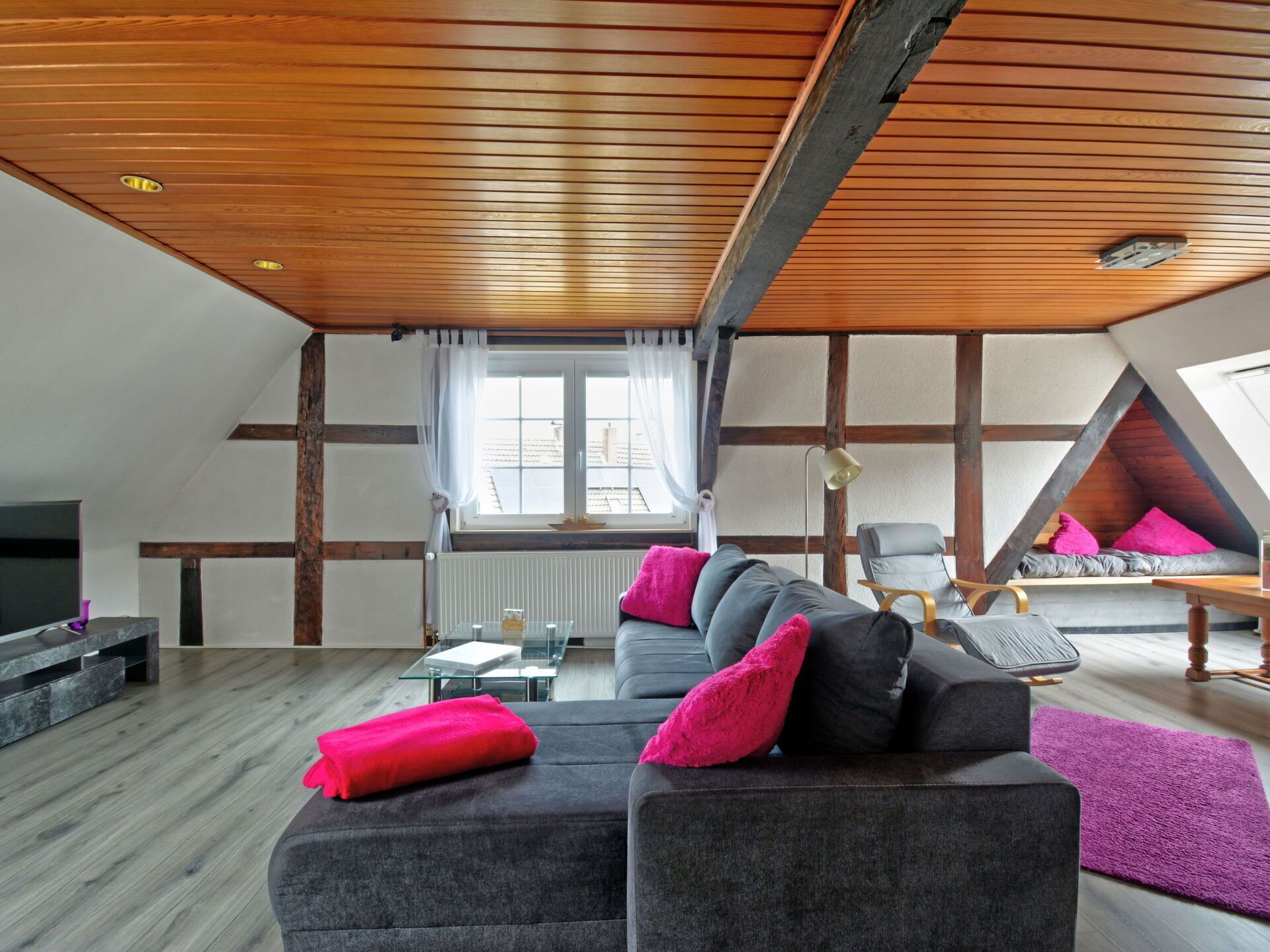 A loft-style living room with a sloped ceiling, a sofa with cushions, a coffee table, a chair, and a window with curtains.