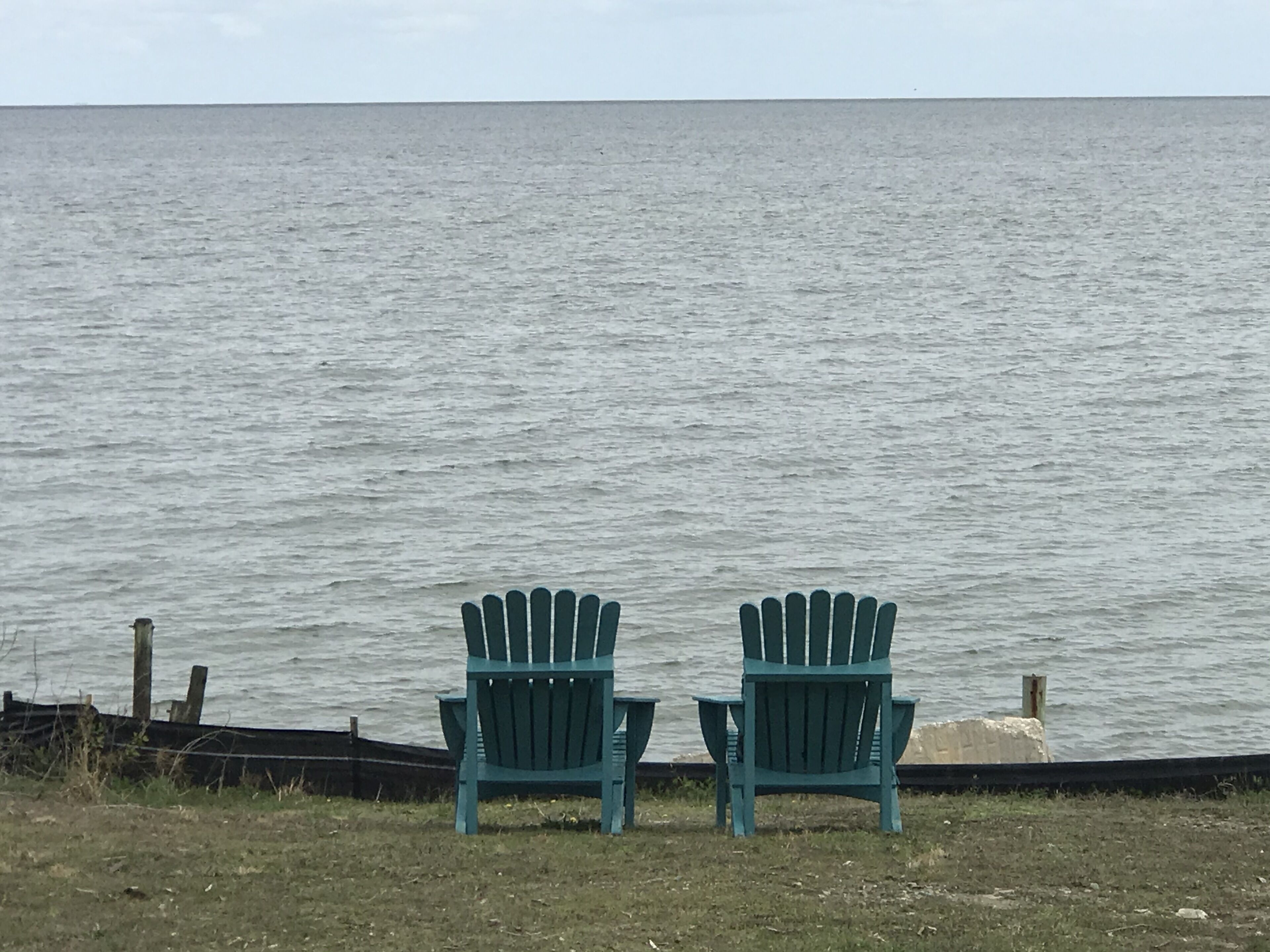 Two green Adirondack chairs facing a body of water.