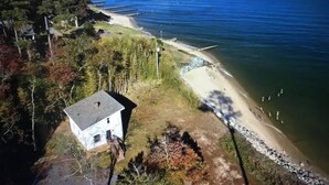 An aerial view of a coastal area with a beach, a small house, and a pier extending into the water.