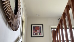A wooden staircase with a handrail, a framed abstract painting on the wall, and a light switch.