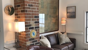 A living room with a brick fireplace, a brown leather sofa, a glass coffee table, and a white shag rug.