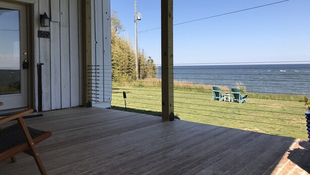 A wooden deck with a view of the ocean, a bench, and a door with a number plate.