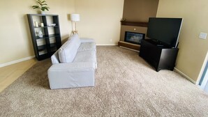 Uma sala de estar com um sofá cinzento, um rack preto, uma televisão, uma lareira e uma estante de livros.