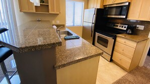 Uma cozinha com bancadas de granito, armários de madeira, geladeira de aço inoxidável, micro-ondas e forno.