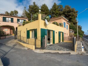 A yellow building with green shutters, a satellite dish, and a stone-paved entrance.