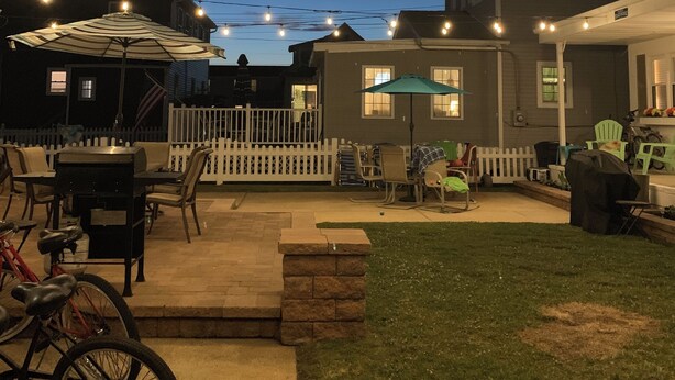 Un giardino sul retro con un'area barbecue, posti a sedere all'aperto e un recinto con tanto di steccato bianco.