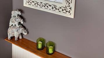 A mirror with an ornate white frame reflecting a bed with pillows and a hanging lamp. Below, a shelf holds decorative items and candles.