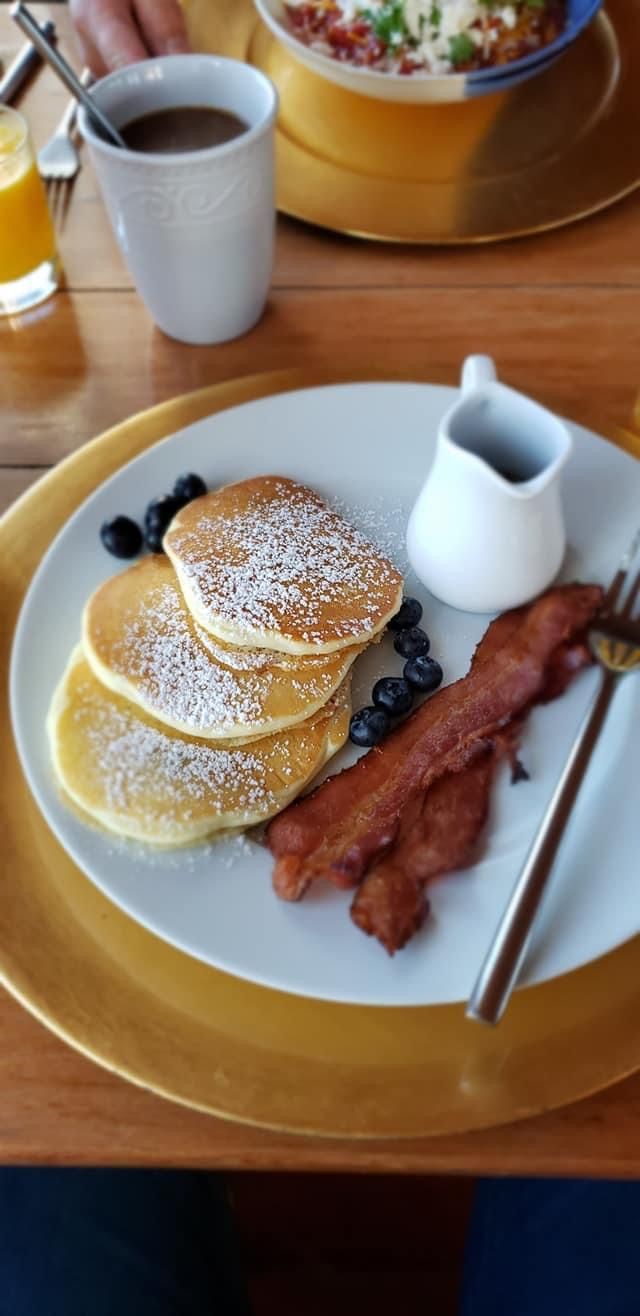 A breakfast plate with pancakes, bacon, blueberries, and a small jug of syrup.