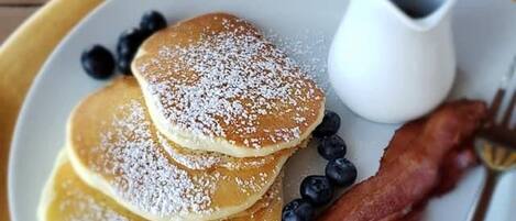 A breakfast plate with pancakes, bacon, blueberries, and a small jug of syrup.