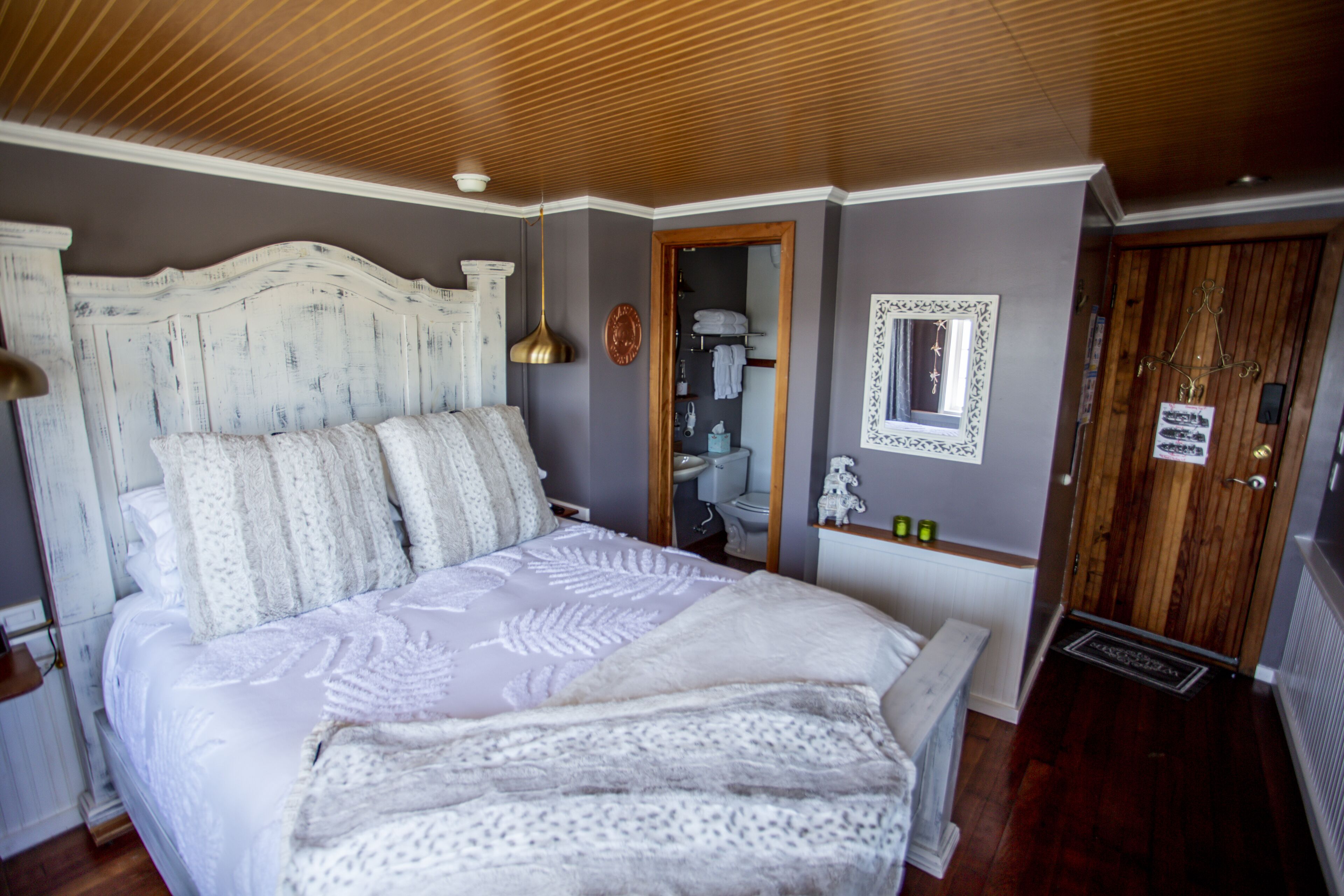 A bedroom with a large bed, wooden headboard, and a mirror on the wall.