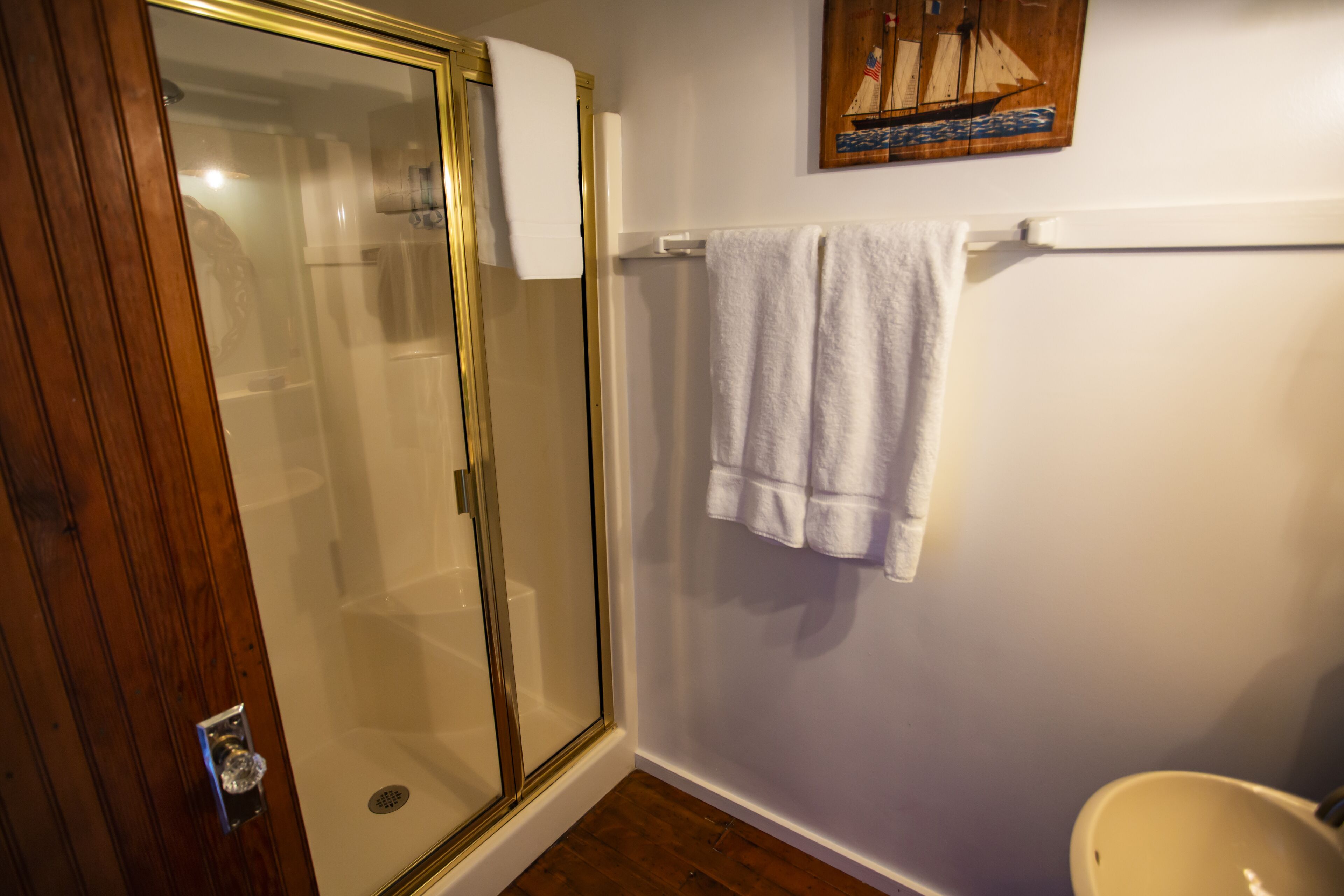 Une salle de bain avec une douche à parois de verre, un lavabo blanc et une porte en bois.