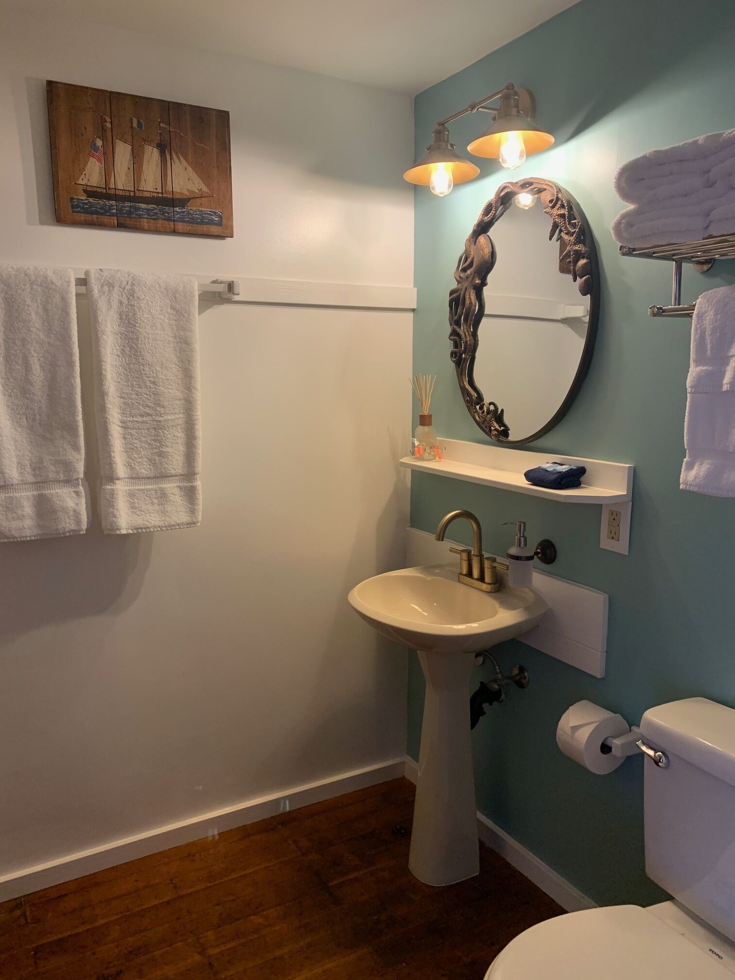 A bathroom with a pedestal sink, a toilet, a towel rack, and a wall-mounted mirror.