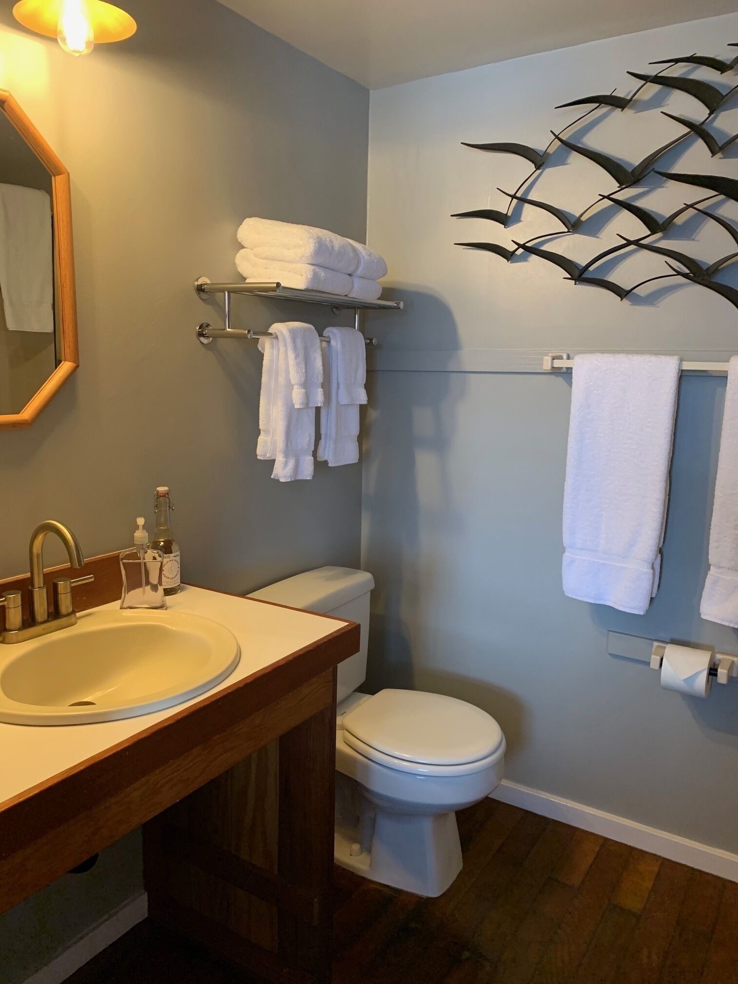 A bathroom with a wooden vanity, a sink, a toilet, and a towel rack with folded towels.