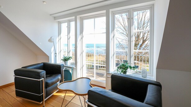A modern living room with a black leather sofa, a small table, and a chair. Large windows offer a view of the outdoors. - Awesome home in Brantevik with sauna (Brantevik)