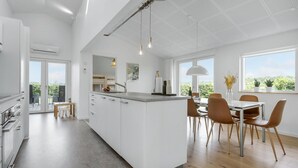 A modern kitchen with a central island, a dining area with chairs, and large windows offering a view of greenery. - Amazing home in Odder with kitchen (Odder)