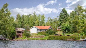 A lakeside property with a main house featuring a red roof, a smaller wooden structure, and lush greenery. - Lovely home in Idkerberget (Idkerberget)