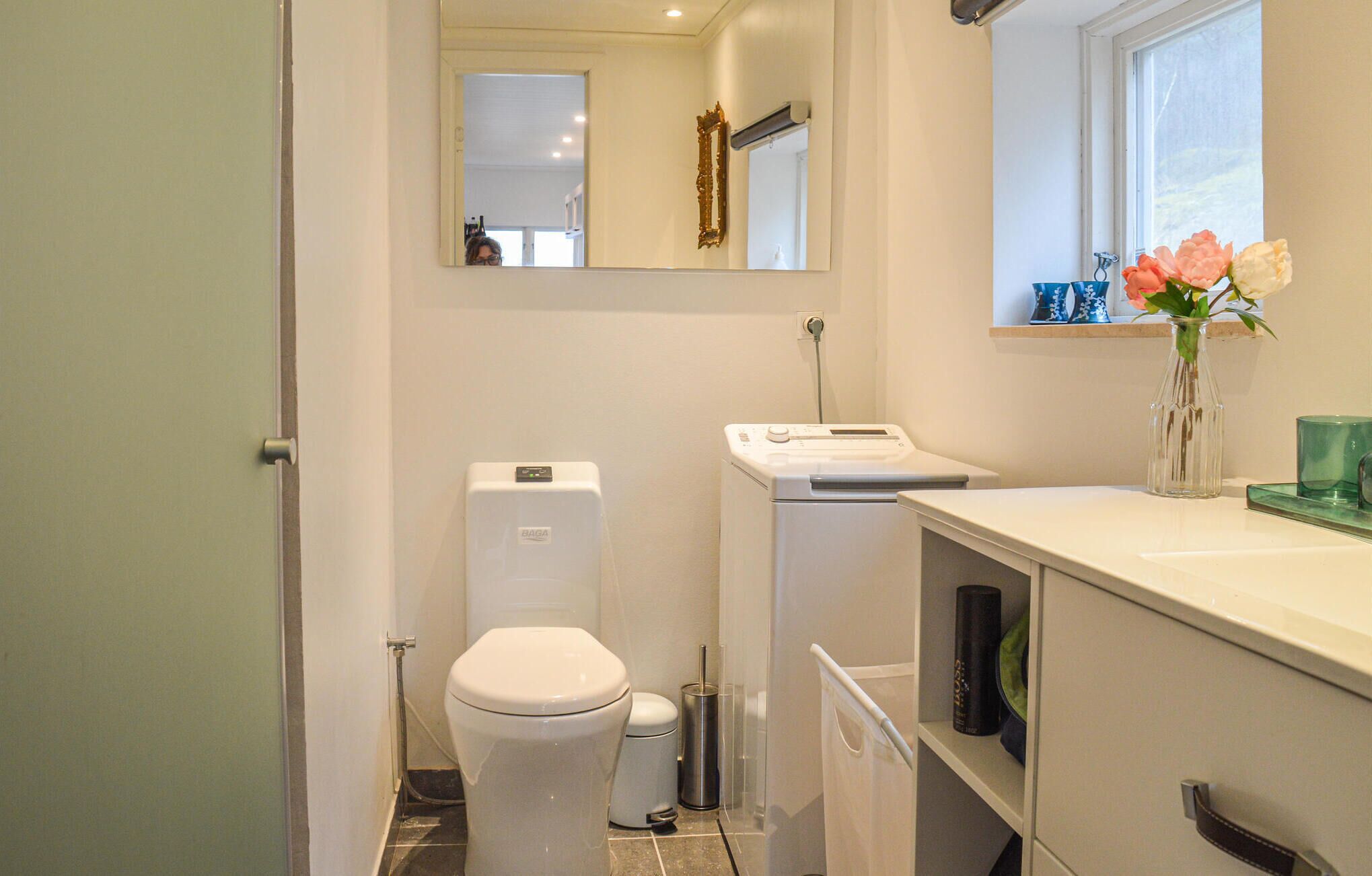 A compact bathroom with a toilet, a washing machine, and a sink area with a vase of flowers.