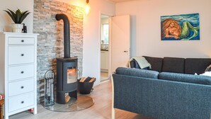 A modern living room with a stone wall, a black wood-burning stove, a grey sofa, and a painting on the wall. - 3 bedroom lovely home in Strömstad (Strömstad)