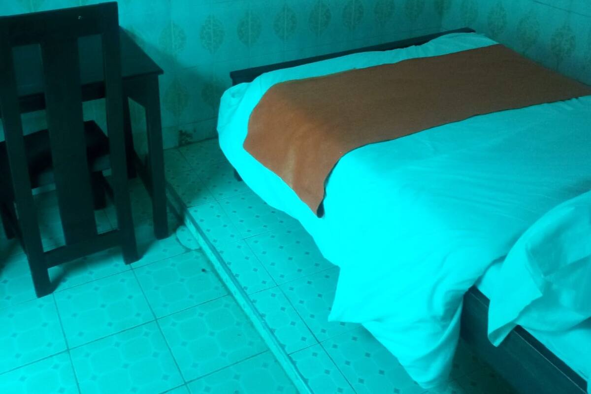 A single bed with a white and brown blanket, a wooden nightstand, and a patterned wall.