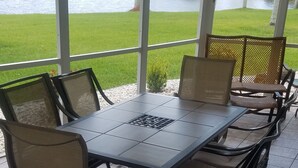 Une terrasse couverte, dotée d’une table et de chaises, qui donne sur une zone herbeuse avec un plan d’eau.