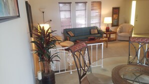 Un salon comprenant un canapé, une table basse et un coin repas avec des chaises. On y trouve également une plante en pot et une lampe sur une table d’appoint.